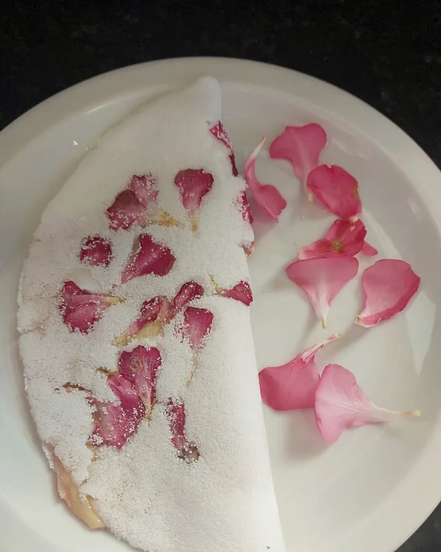 Tapioca dobrada com pétalas cor-de-rosa prensadas na massa, em prato branco.